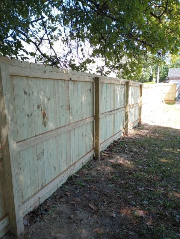 Wooden fence in a yard; green boards, wooden posts, sunlight, grass.