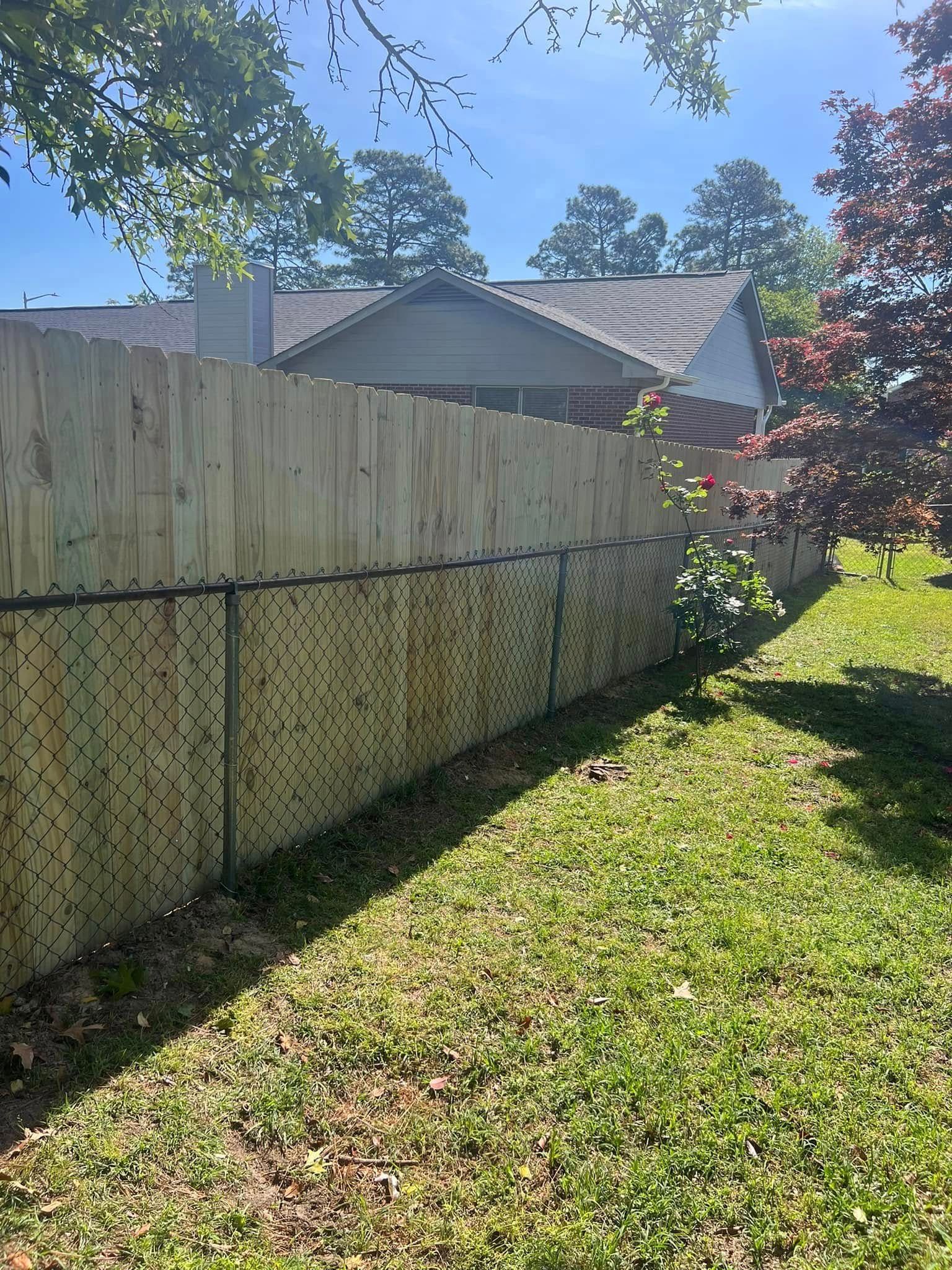 Wooden fence and chain-link fence in a yard, with a house in the background. Green grass.