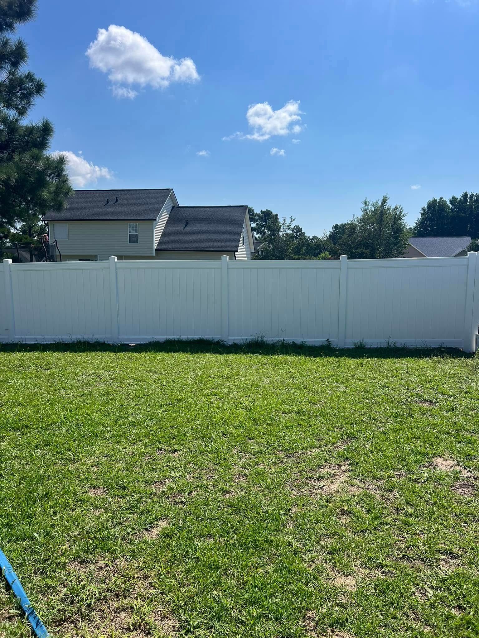 A white fence surrounds a green grassy backyard under a blue sky with puffy clouds.