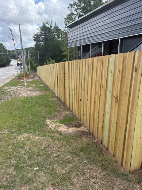 Wooden fence bordering a grassy area, next to a building and road.