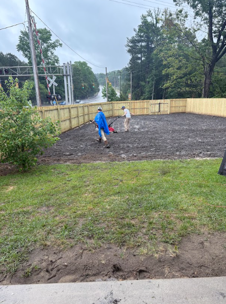 Two people working in a prepared yard with a new wooden fence. Overcast day.
