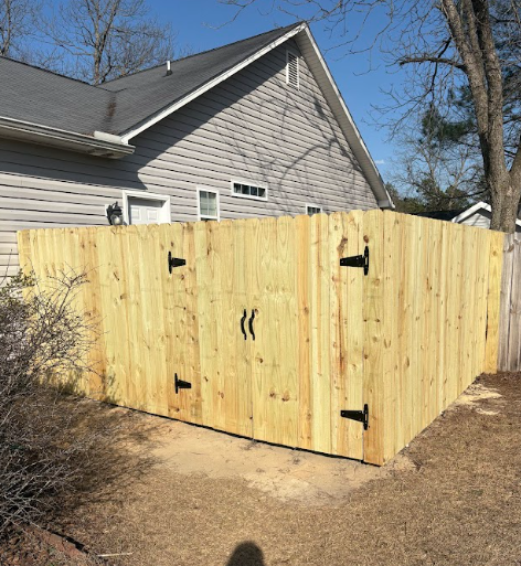 Wooden fence enclosure next to a house, with a gate and black hinges and handles.