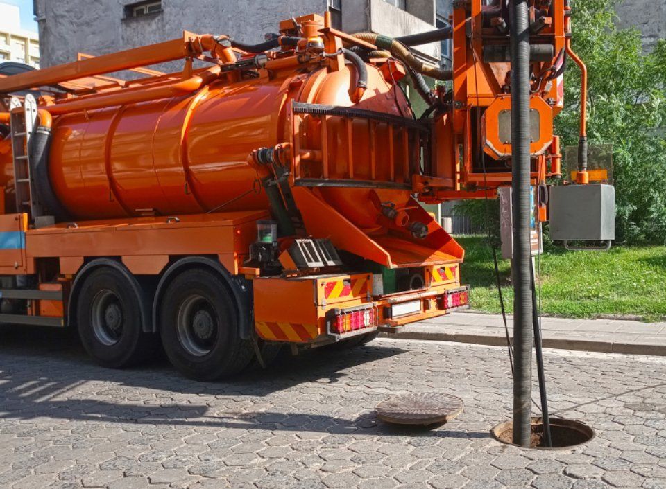 Un camion dell'aspirapolvere arancione sta pulendo un tombino sul lato della strada.