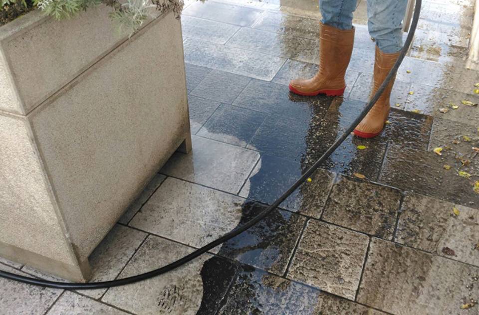 Una persona sta pulendo un pavimento piastrellato con un tubo flessibile.