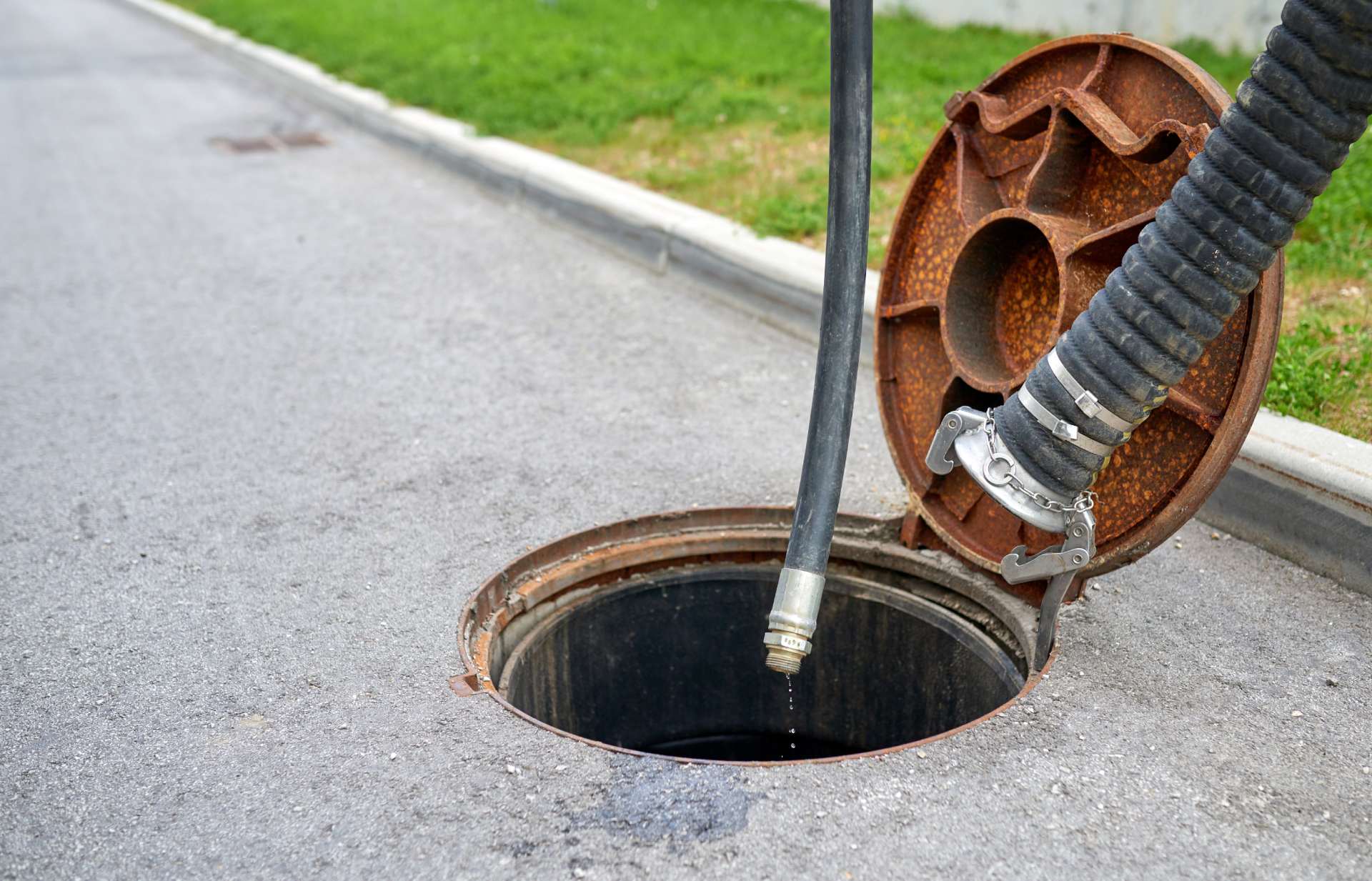 Un tombino è aperto e da esso esce un tubo.