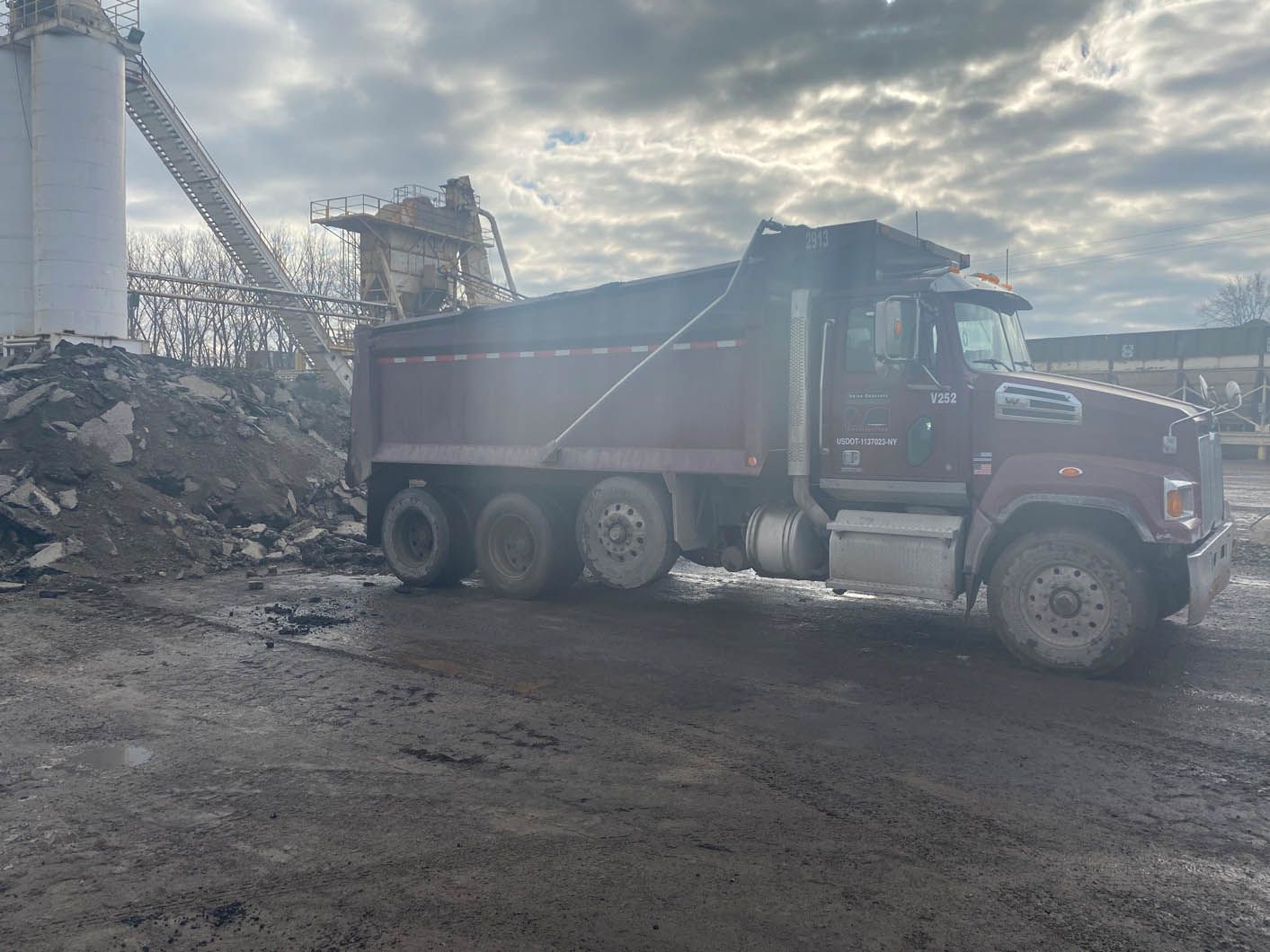 A red dump truck is parked in a dirt lot next to a pile of dirt.