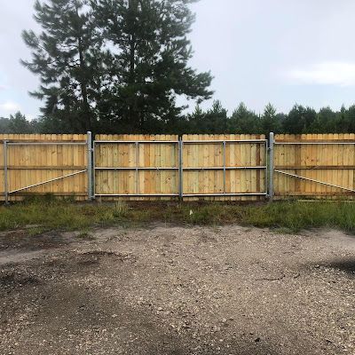 A wooden fence with a metal gate is surrounded by grass and trees.