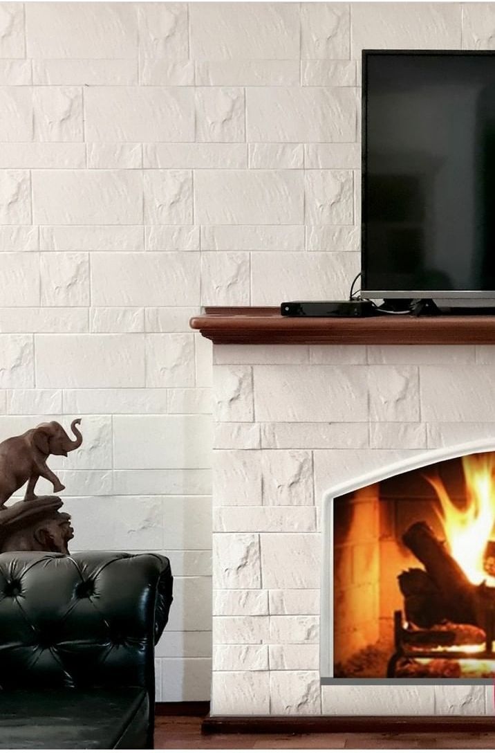 Chimenea con fuego encendido, TV encima, pared de ladrillo blanco y sofá de cuero con estatua de elefante.