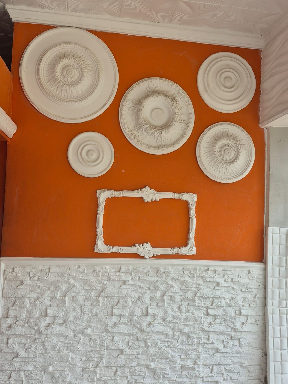 Pared naranja con círculos decorativos y marco blancos, mitad inferior de piedra blanca y moldura blanca.