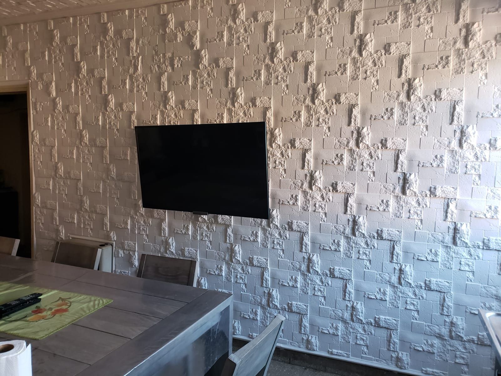 Una pared con textura gris con un televisor negro montado encima de una mesa de comedor.