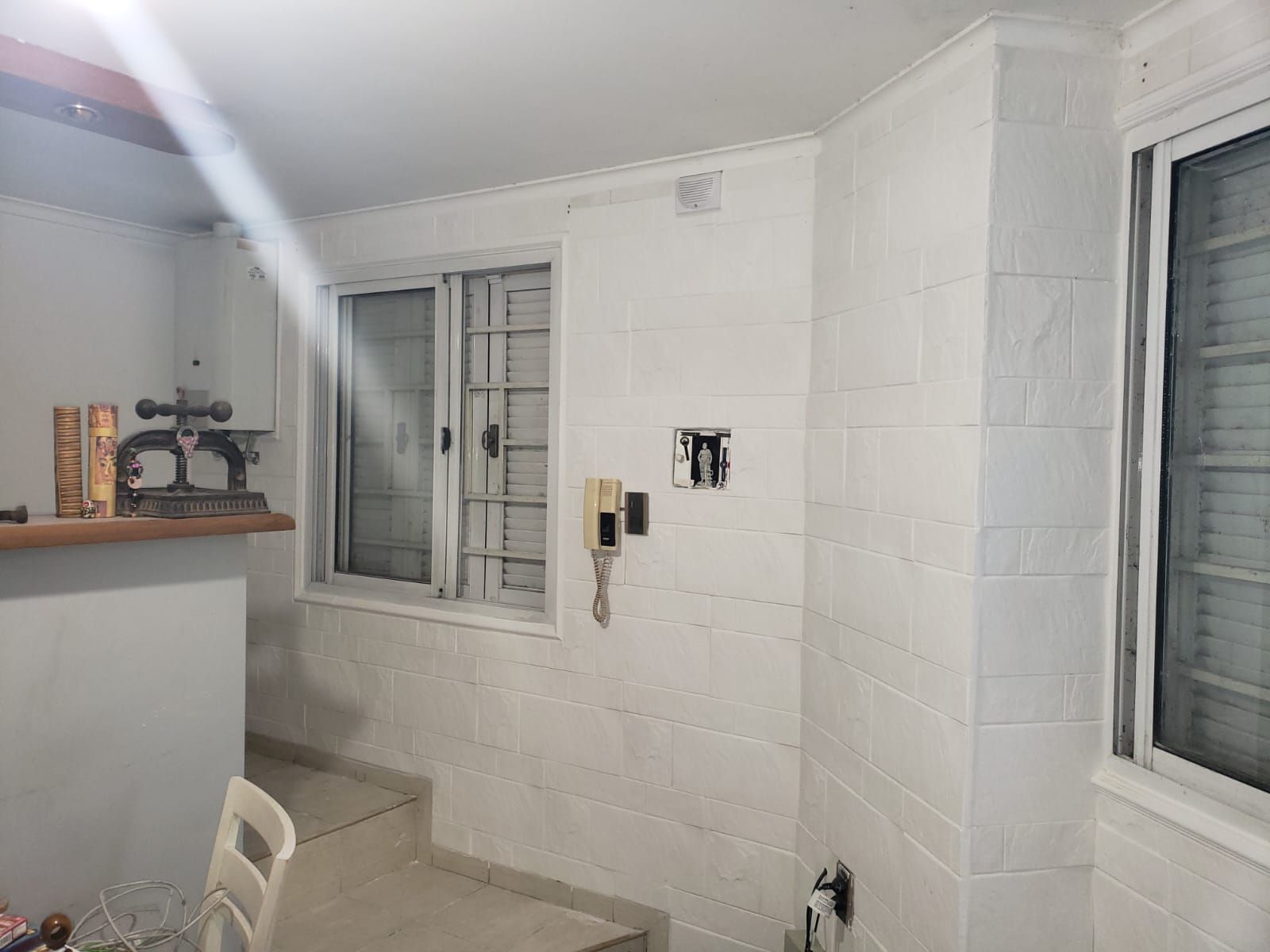 Paredes de azulejos blancos y ventana en una habitación con una lámpara y una encimera parcialmente visible.