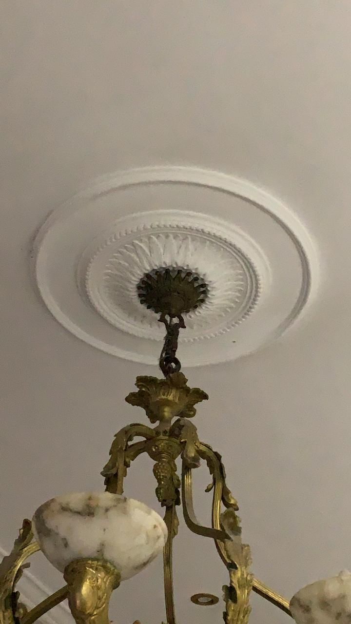 Lámpara de araña de latón antiguo que cuelga de un techo blanco con un rosetón decorativo.