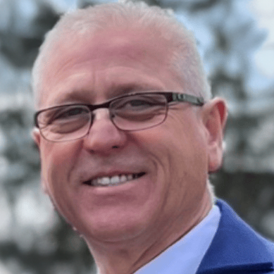 A man wearing glasses and a blue jacket is smiling for the camera.