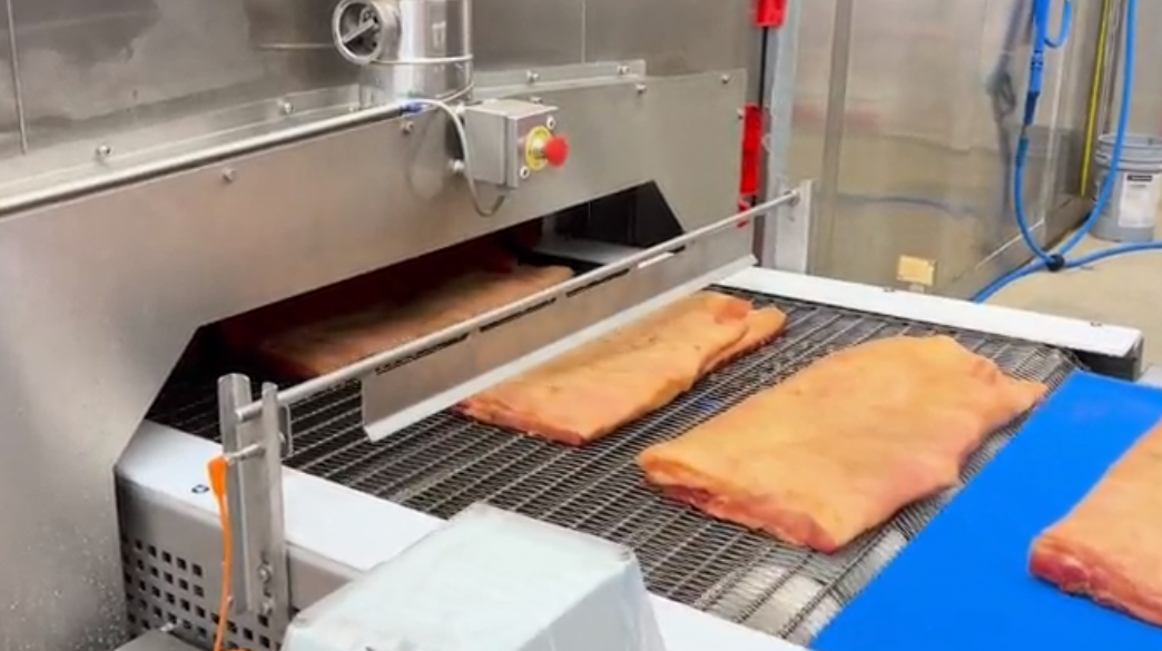 Meat is being cooked on a conveyor belt in a kitchen.