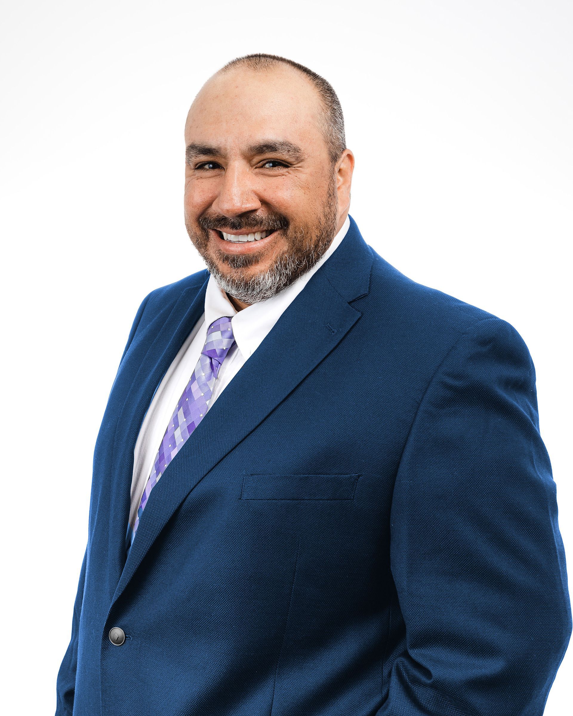 A man in a blue suit and purple tie is smiling.