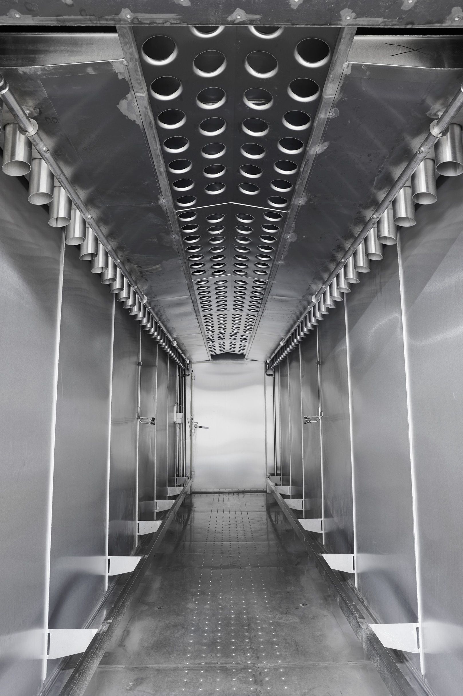 A black and white photo of a long hallway with stainless steel walls.