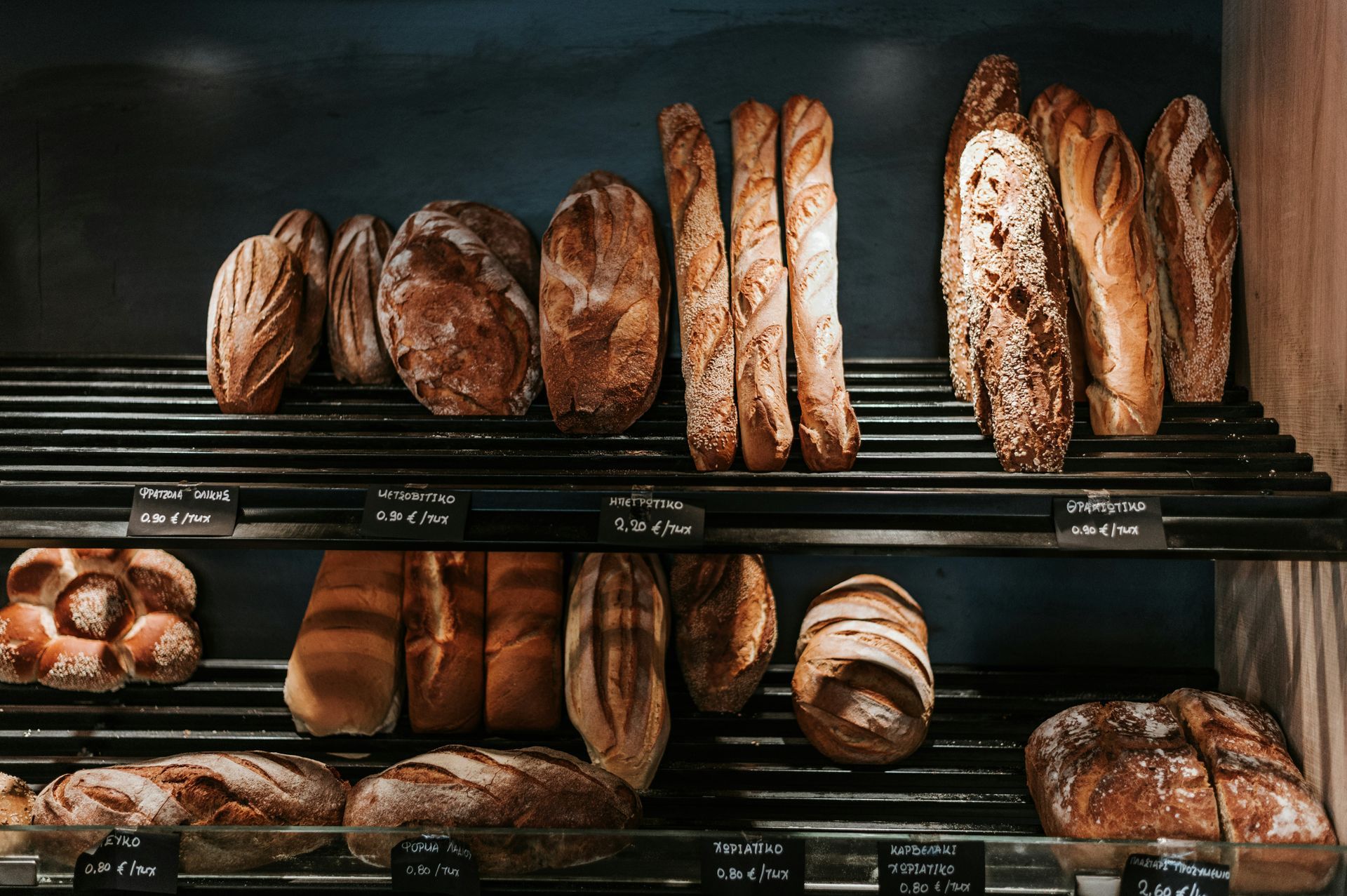 A variety of breads are displayed on a shelf in a bakery.