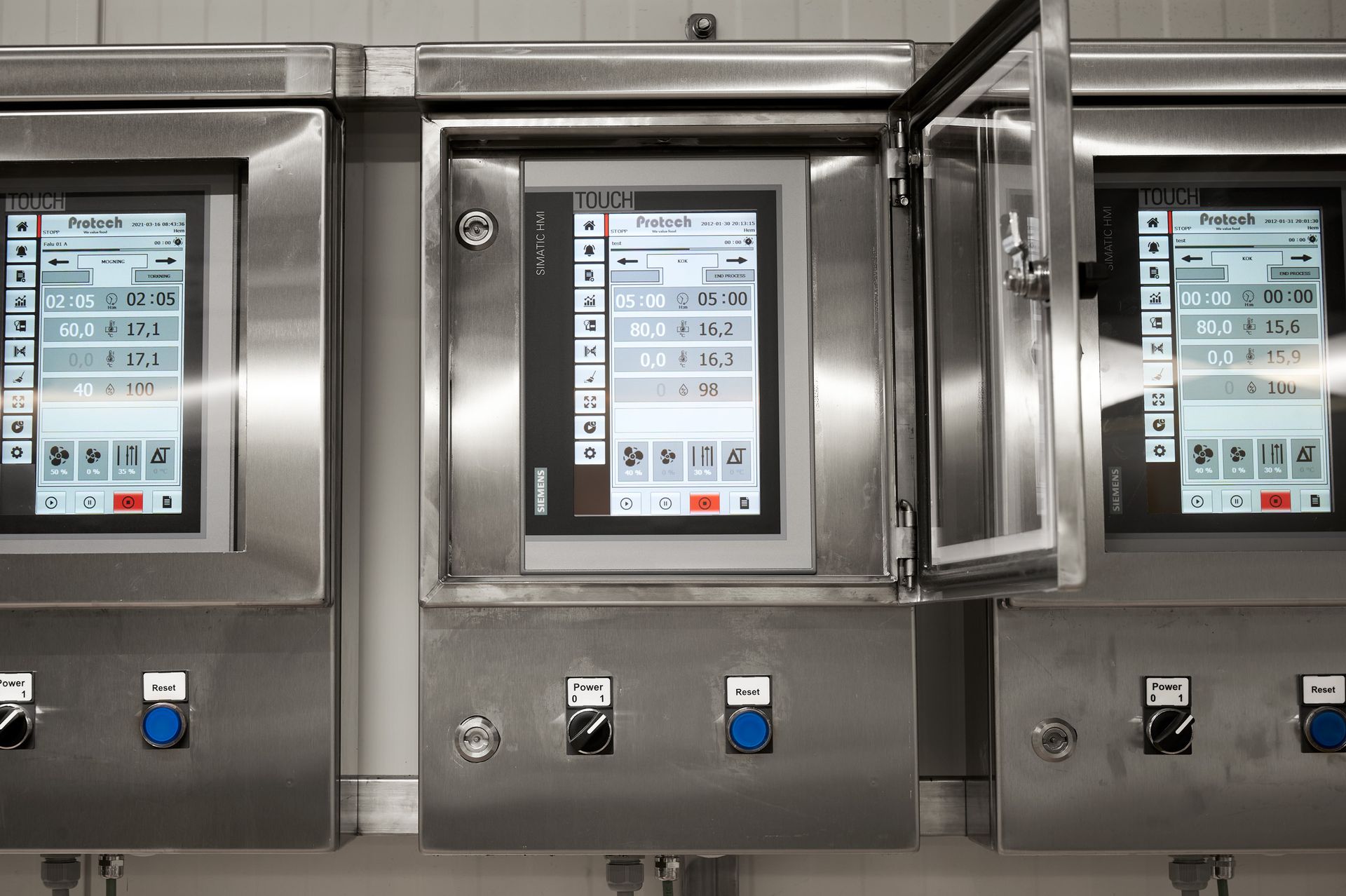 A row of stainless steel control panels with a few monitors on them