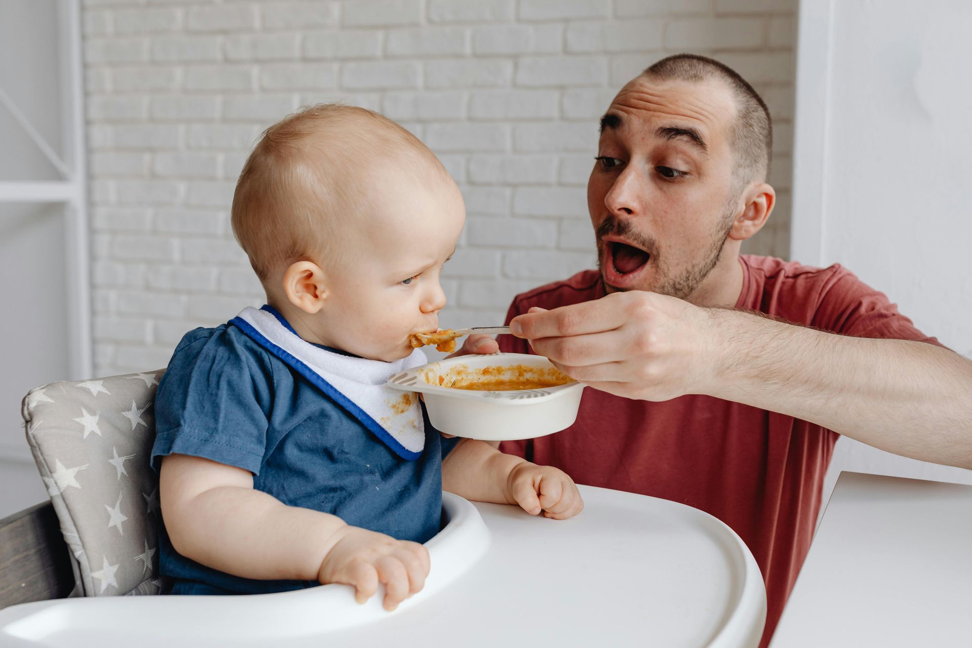 A man is feeding a baby in a high chair with a spoon.