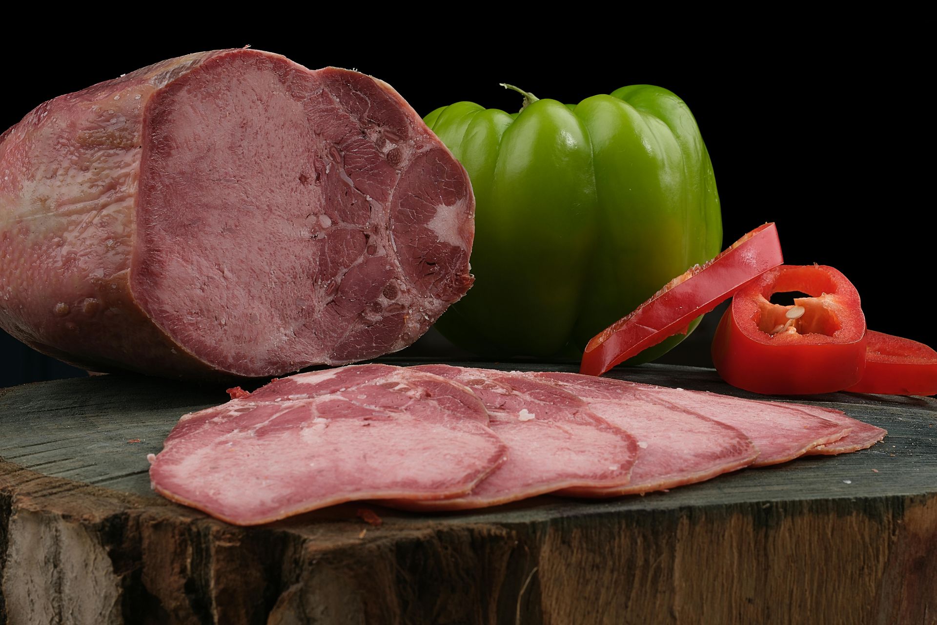 A piece of meat is sitting on a cutting board next to peppers and tomatoes.