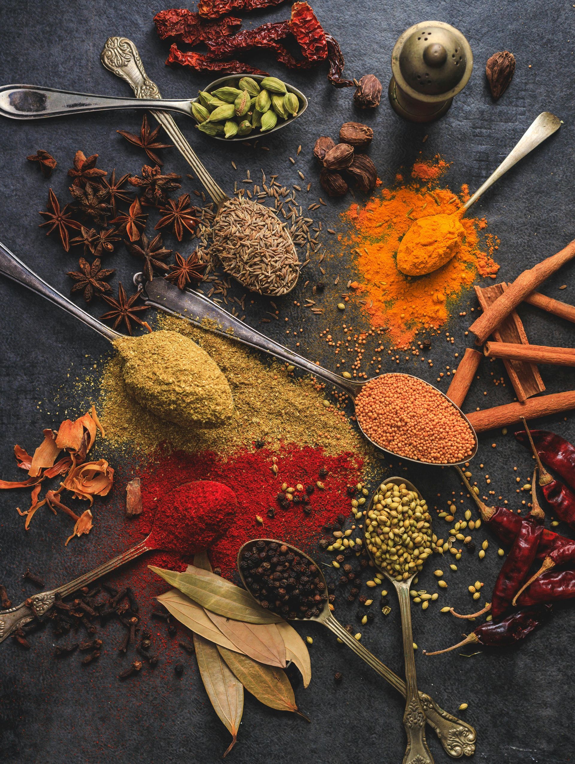 There are many different types of spices in spoons on the table.