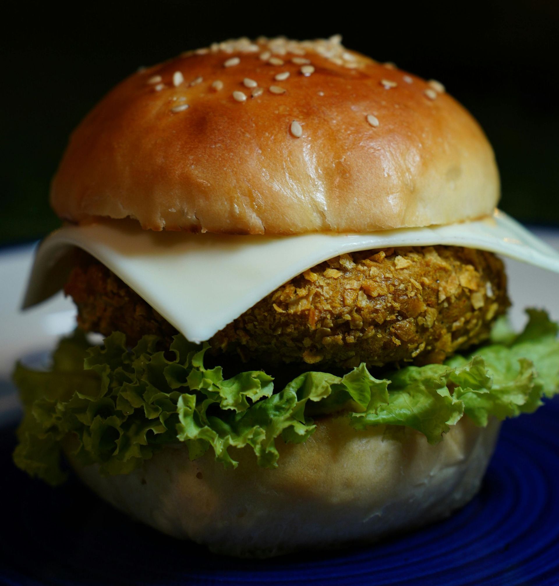 A close up of a hamburger with lettuce and cheese on a blue plate