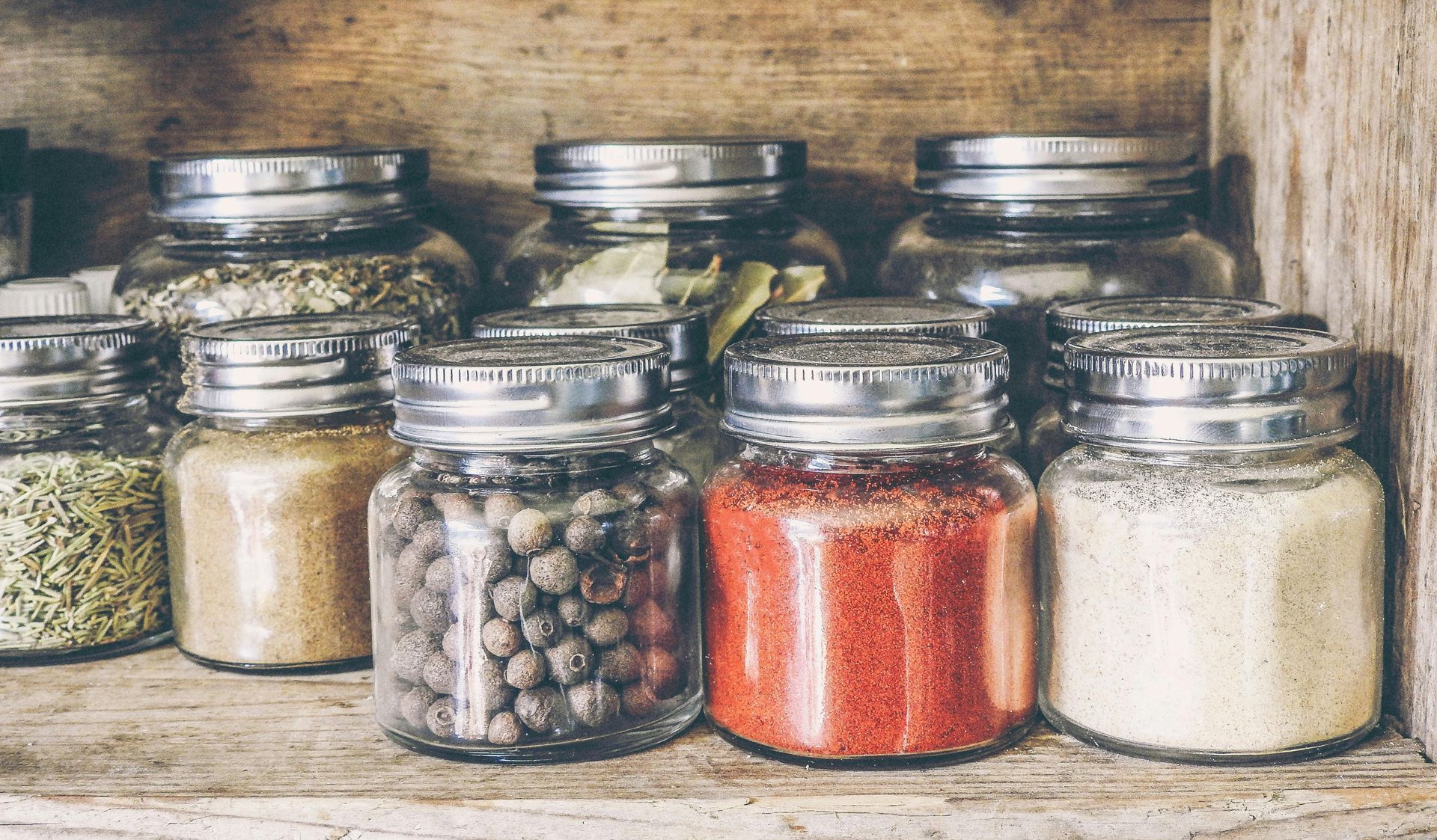 A wooden shelf filled with jars filled with different types of spices.