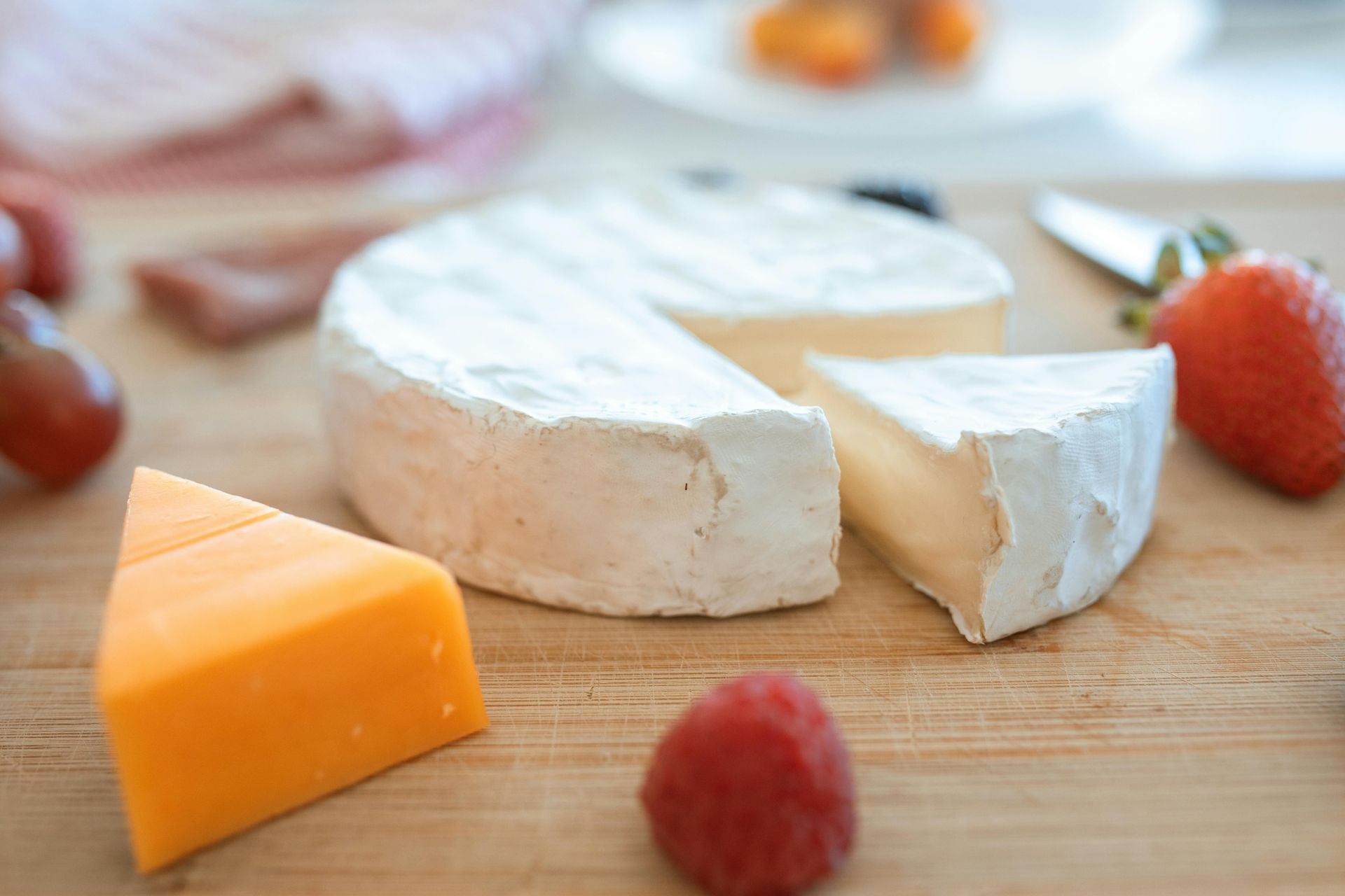 A cutting board topped with cheese , raspberries and grapes.