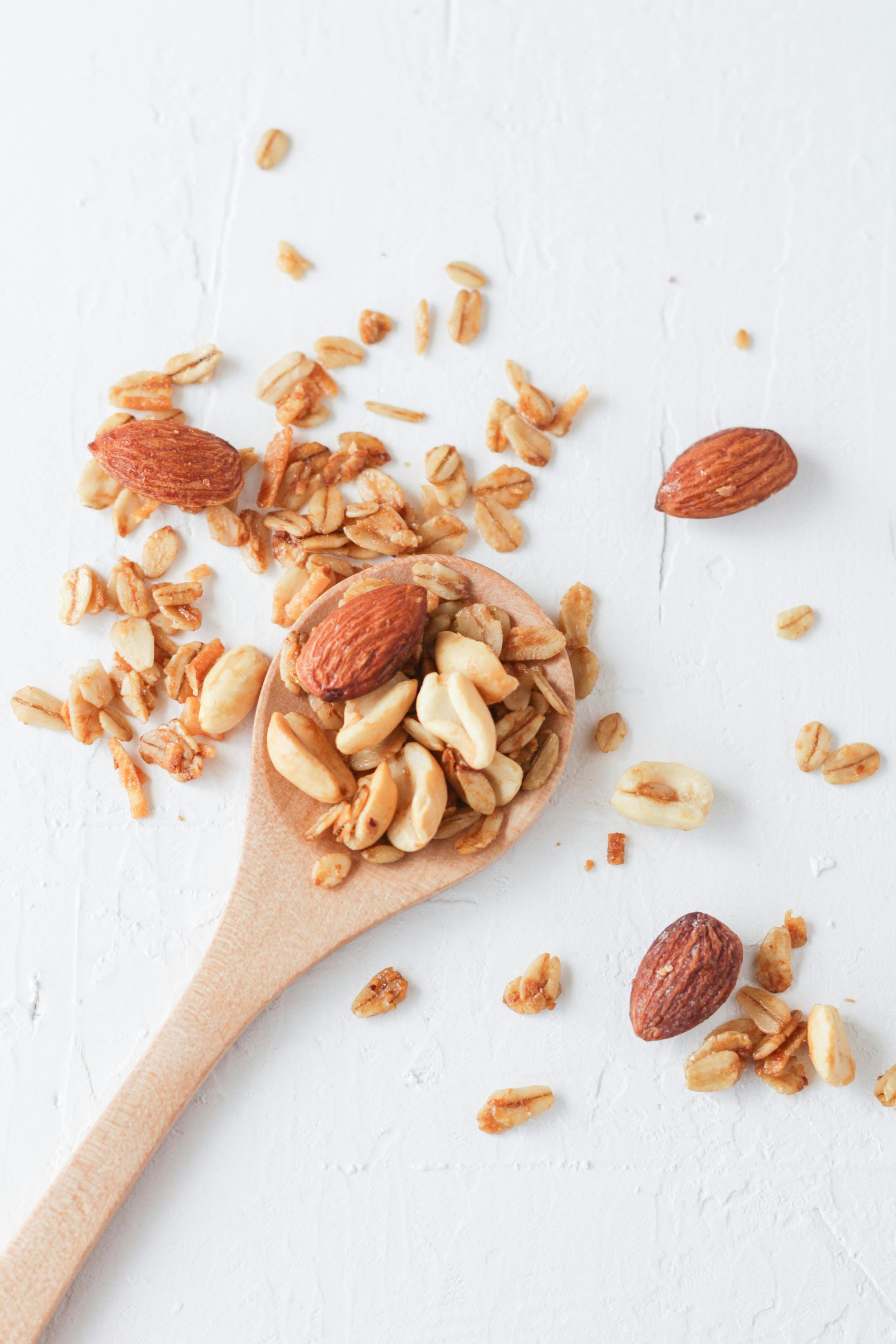 A wooden spoon filled with nuts and granola on a white surface.