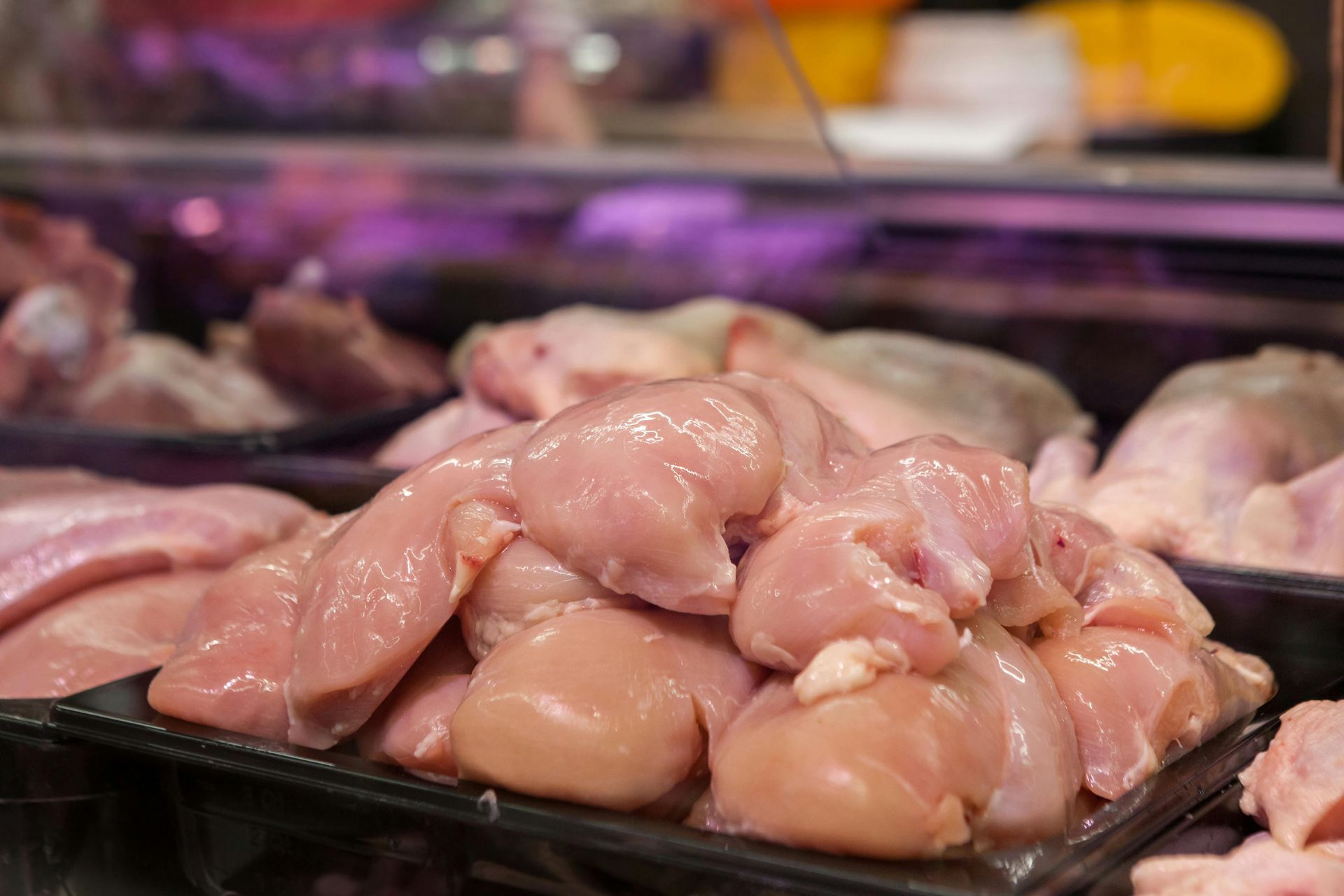 A pile of raw chicken breasts on a tray in a butcher shop.