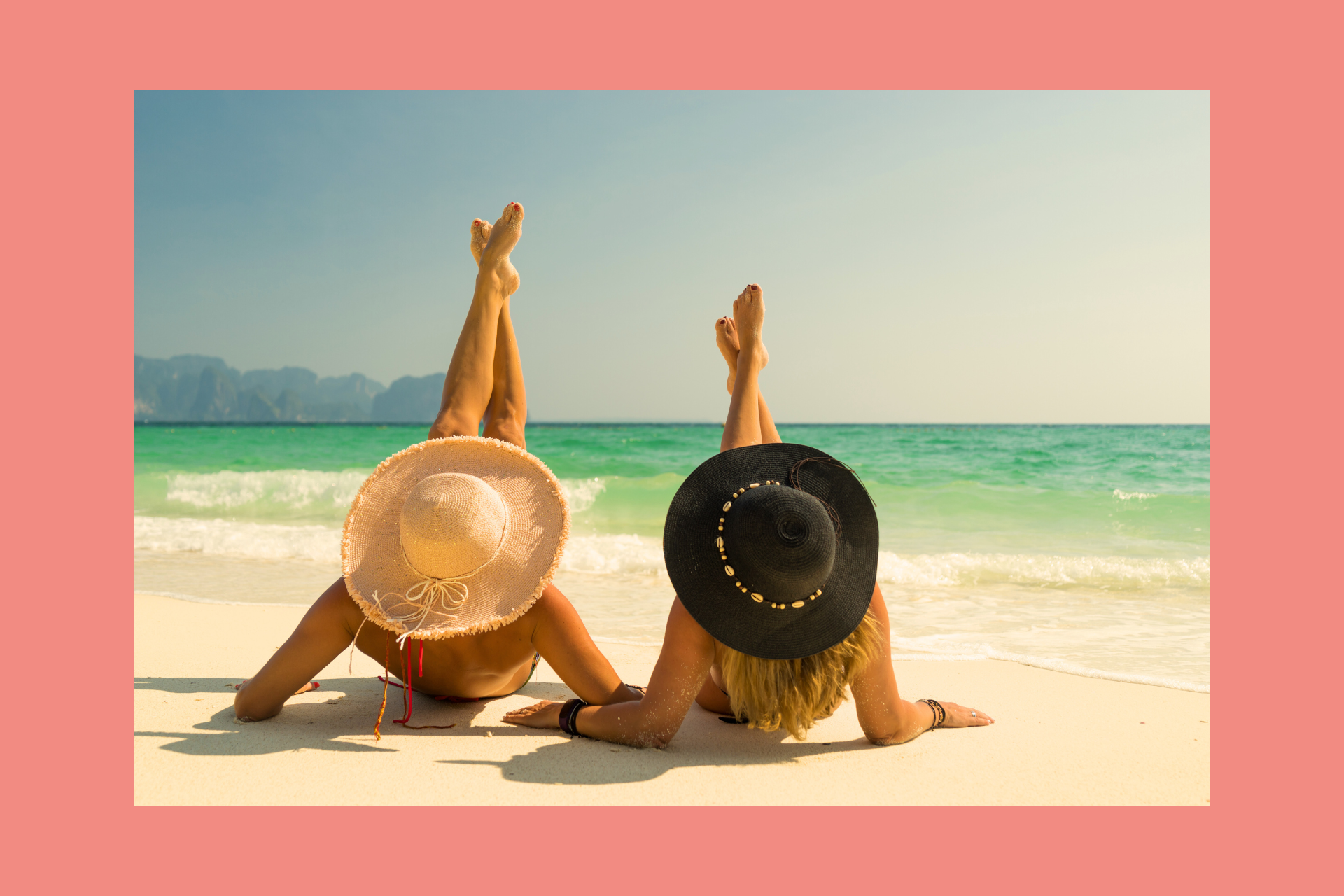 Two women are laying on their stomachs on the beach.