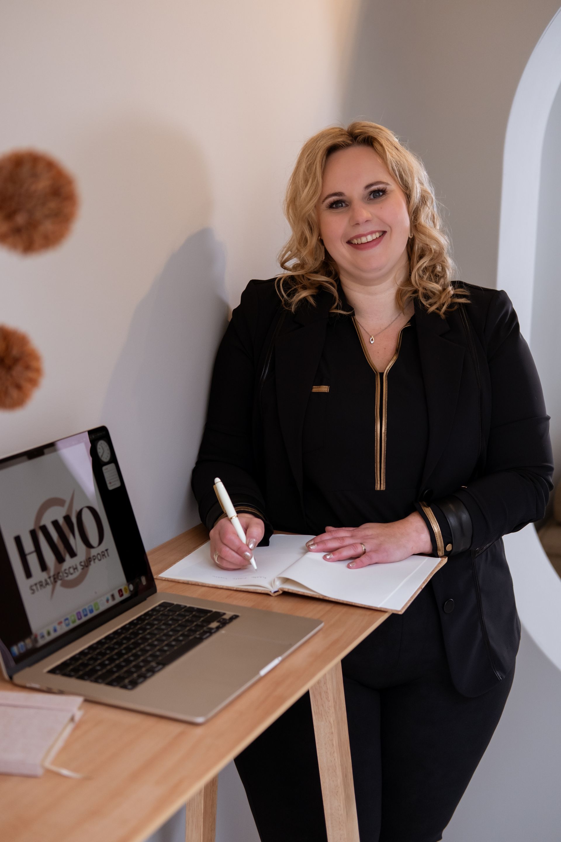 Laptop, notitieboek, telefoon en bril op een bureau; handen die typen op de computer.