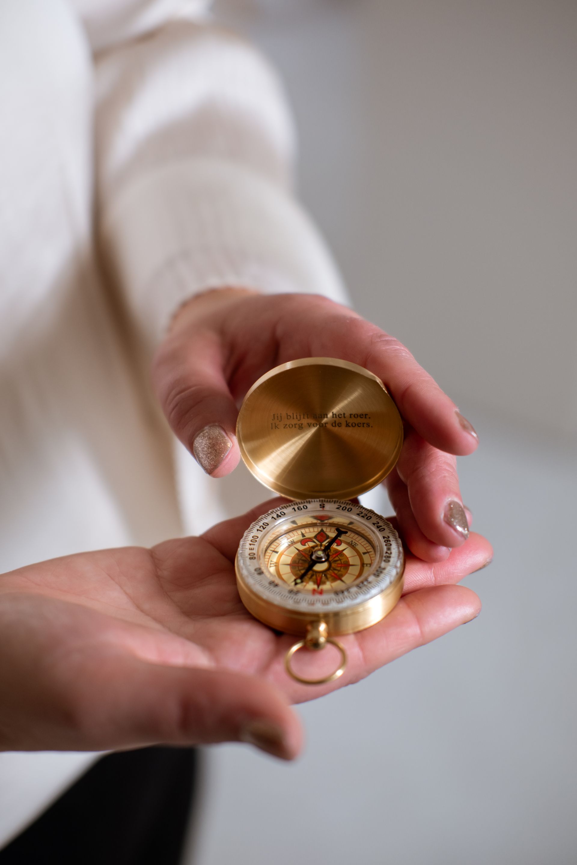 Vrouw in zwarte blazer en broek zit glimlachend op een stoel, binnen.