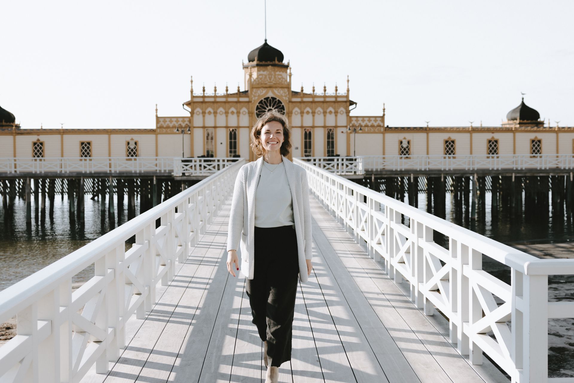 Kvinna i kavaj går mot en utsmyckad pirbyggnad; solig dag.