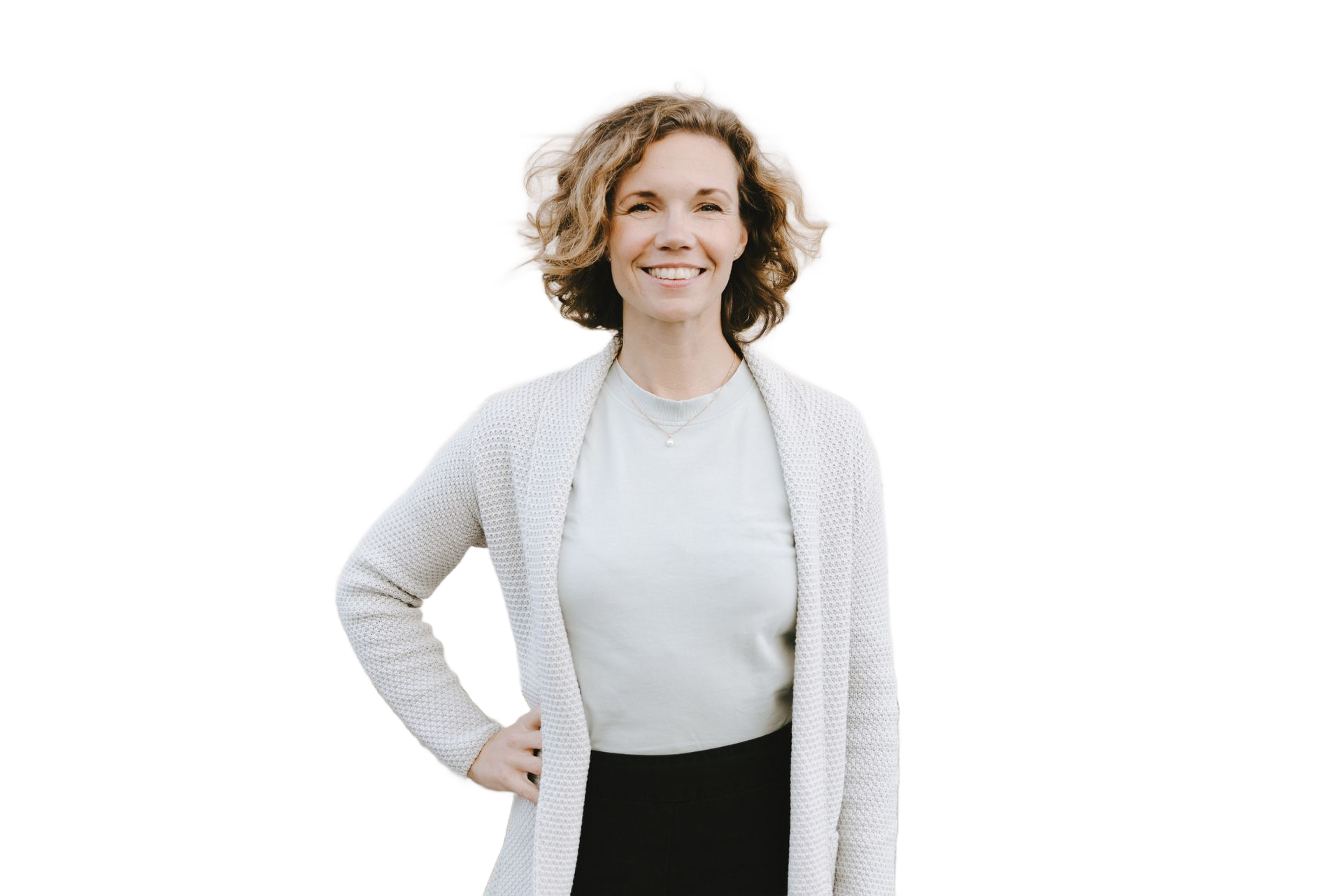 Kvinna med lockigt brunt hår ler, handen på höften. Klädd i vit kofta, ljusgrön skjorta och svart kjol.