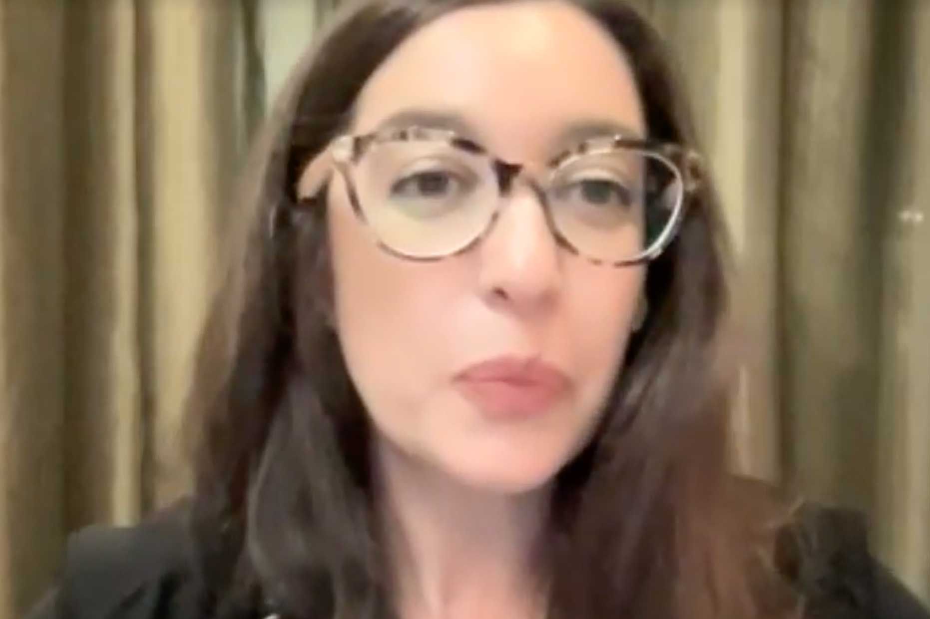 Lynn Zovighian wearing glasses, looking forward, with long dark hair, wearing a black blazer.