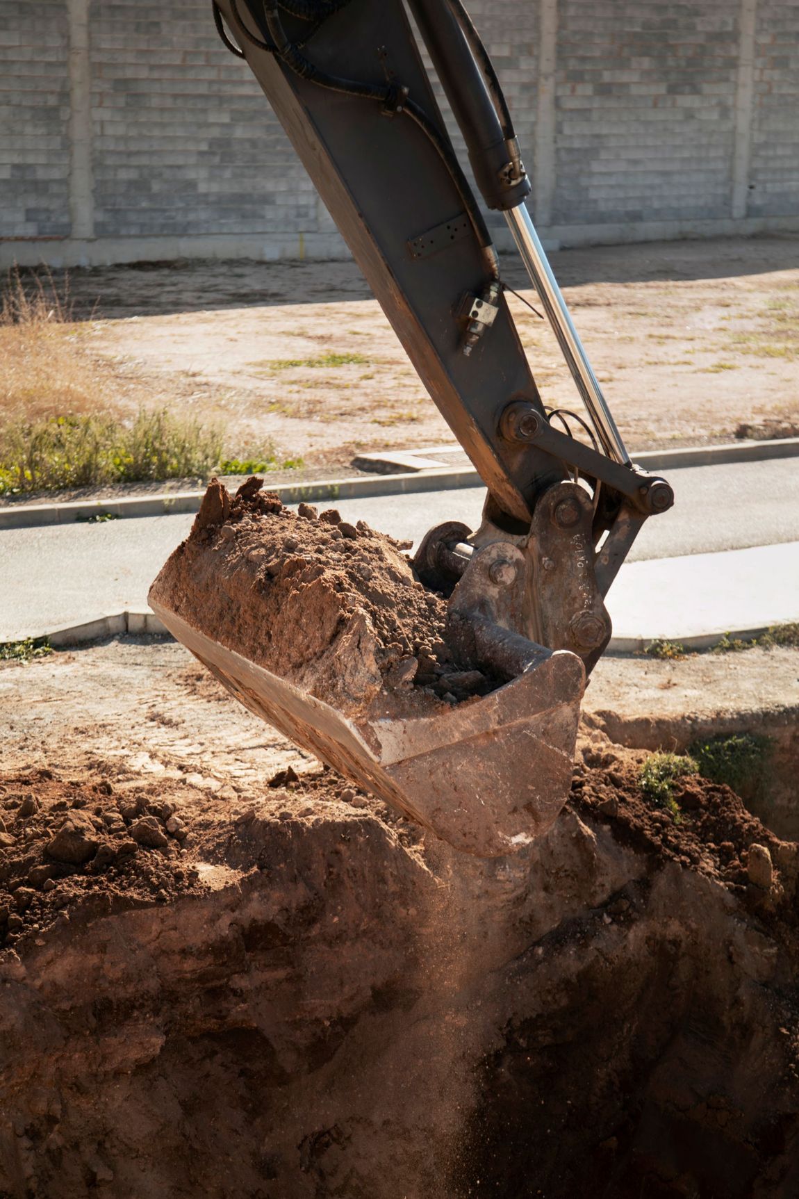 Excavator bucket digging into the ground; dirt and dust flying.