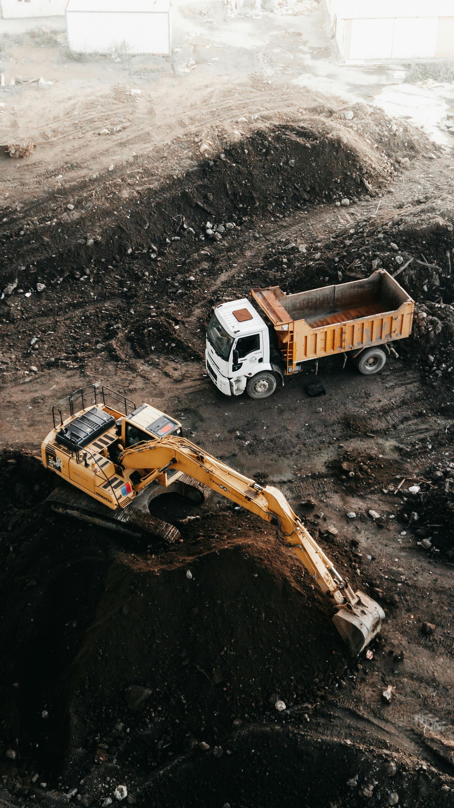 Yellow excavator loading a dump truck with dirt at a construction site.