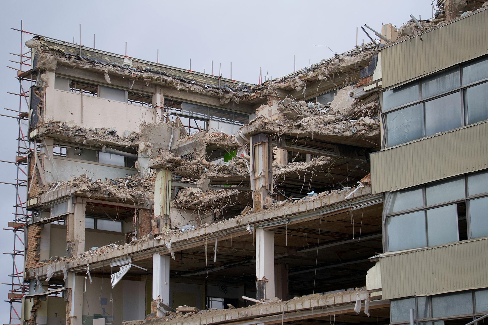 Partially demolished multi-story building with exposed concrete and debris, scaffolding on the left.