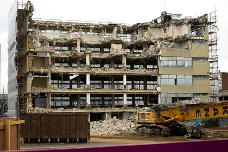 Building demolition; a large excavator tears down a multi-story structure.