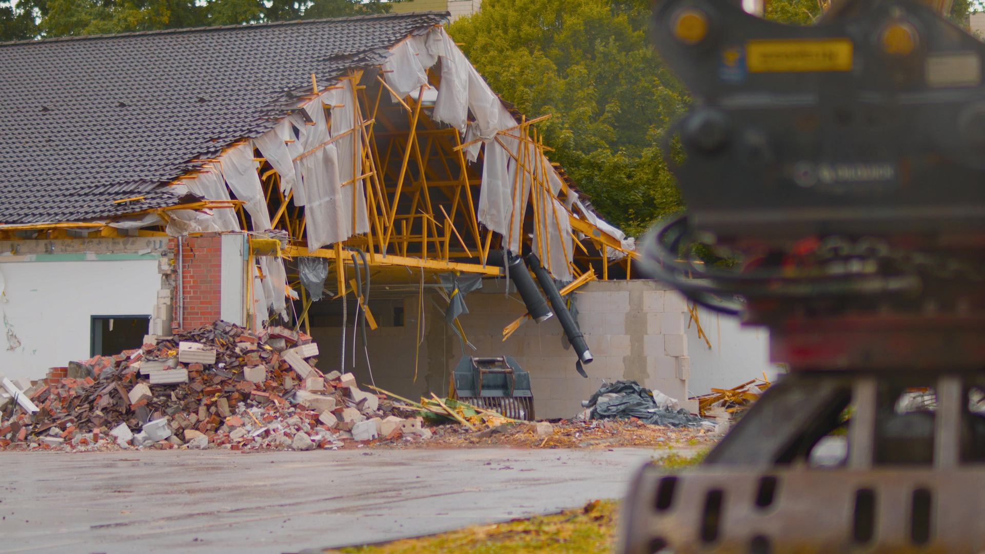 Demolition of a building in progress; excavator arm, rubble, exposed roof supports.