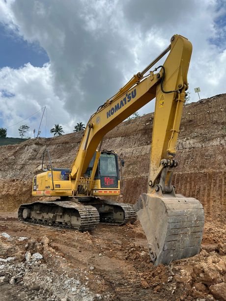 Yellow Komatsu excavator digging into a dirt hill under a cloudy sky.