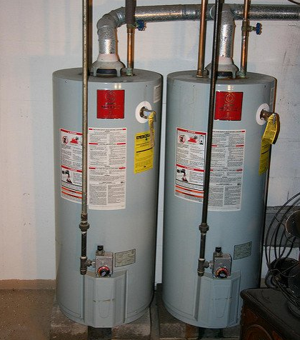 two water heaters are sitting next to each other in a basement .
