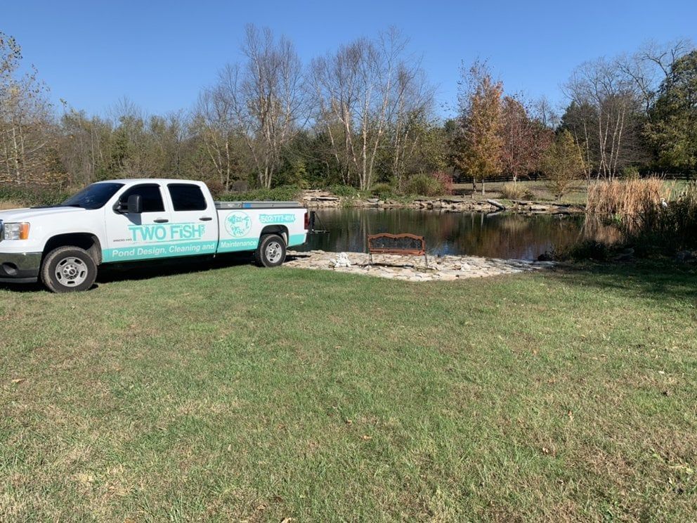 A white truck is parked in a grassy field next to a lake.