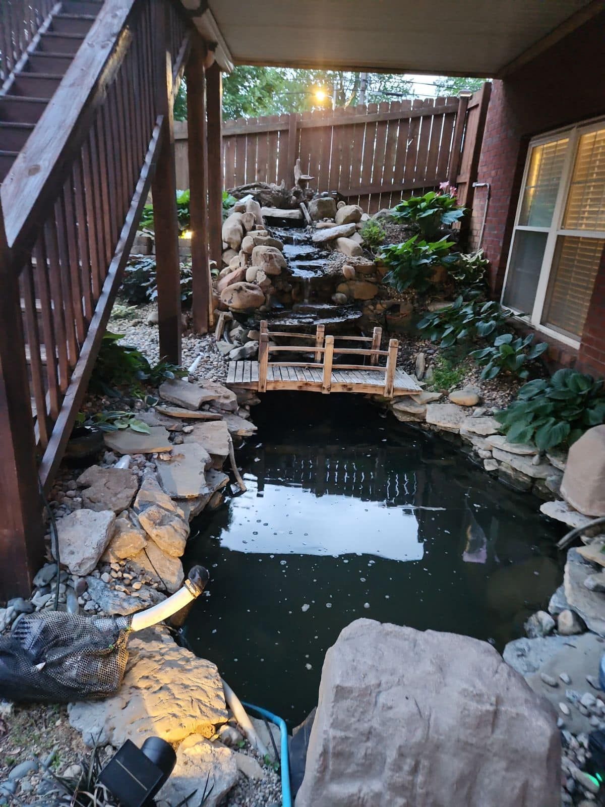 A pond with a waterfall in the backyard of a house.