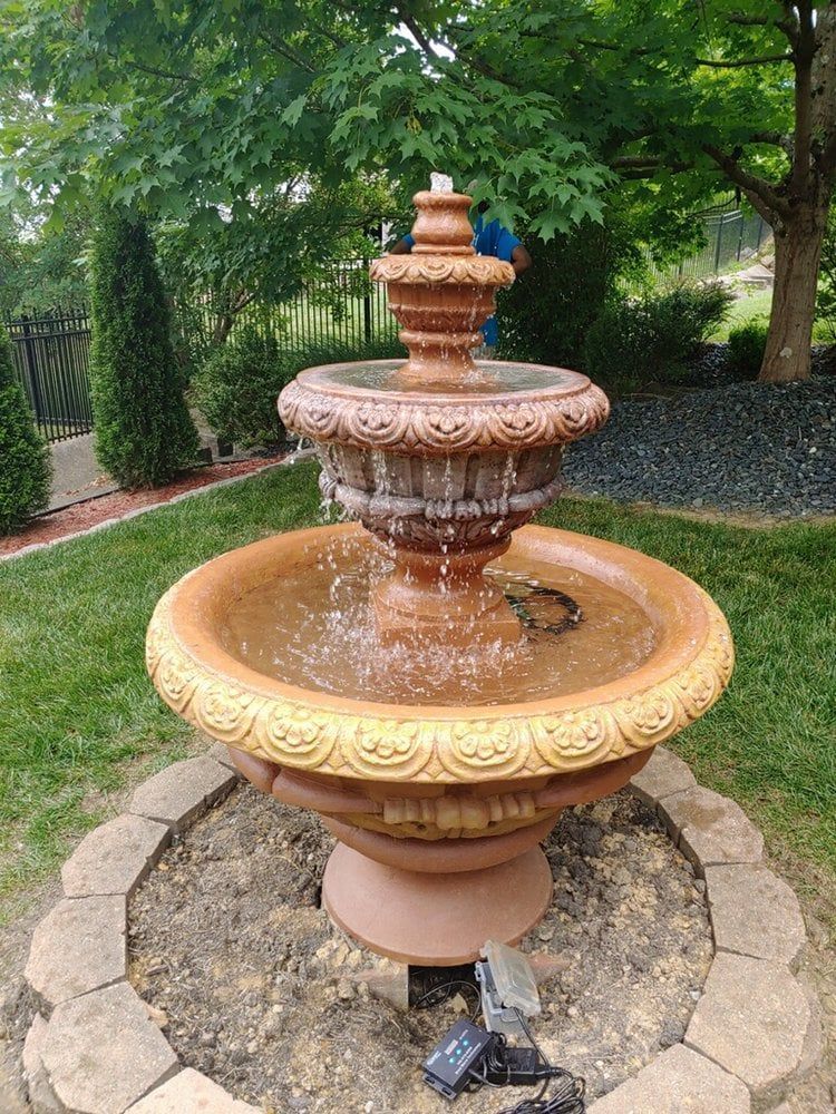 A large fountain is sitting in the middle of a lush green yard.