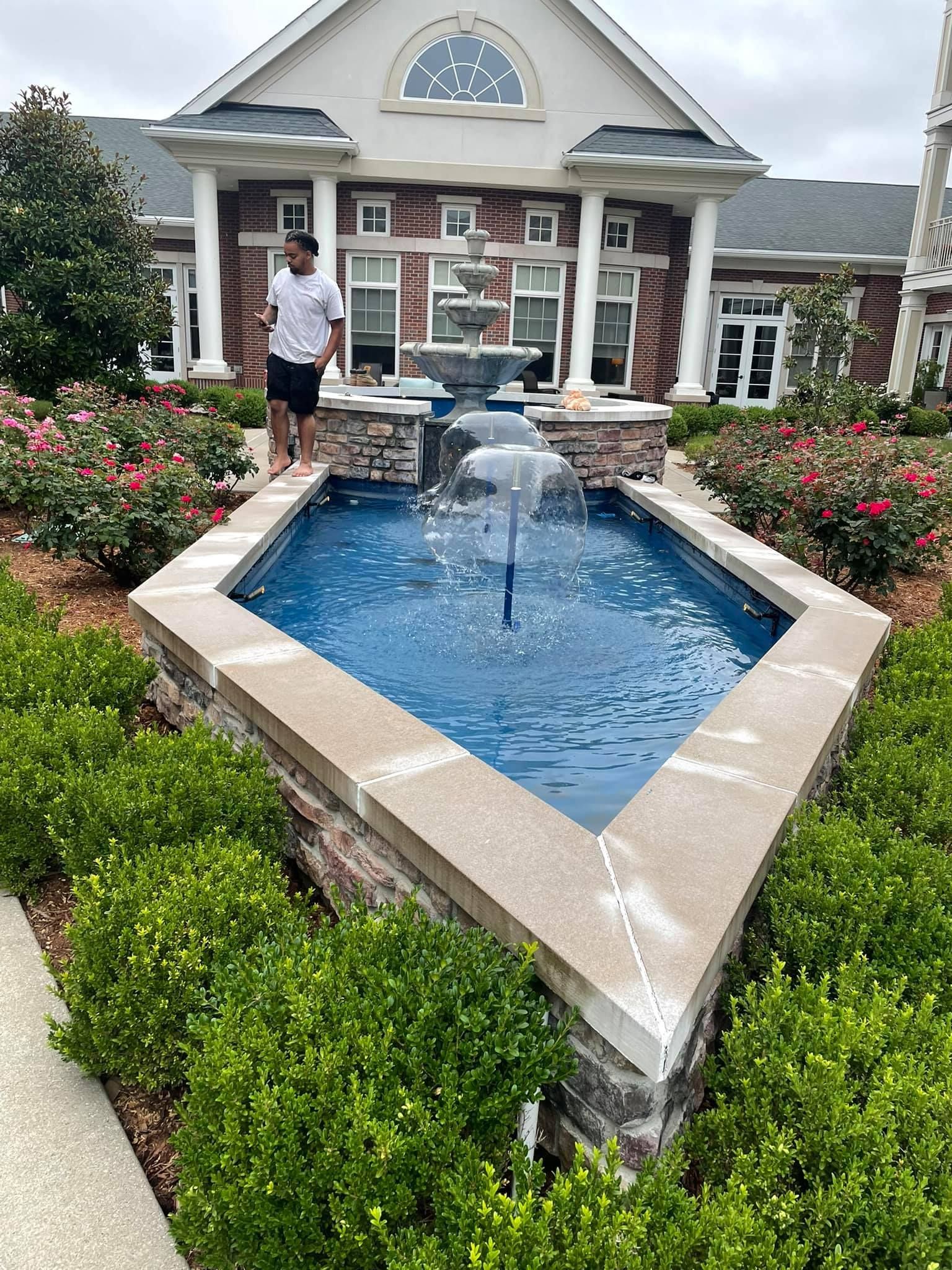 A man is standing next to a fountain in front of a house.
