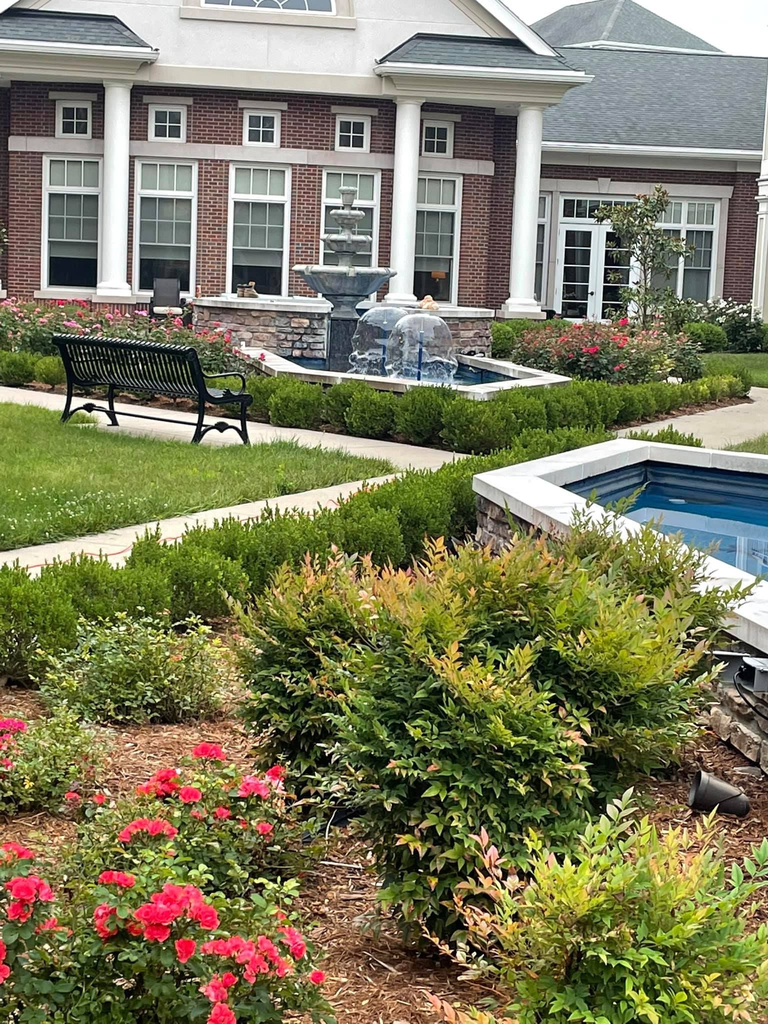 A large brick house with a fountain in the backyard and a bench in front of it.