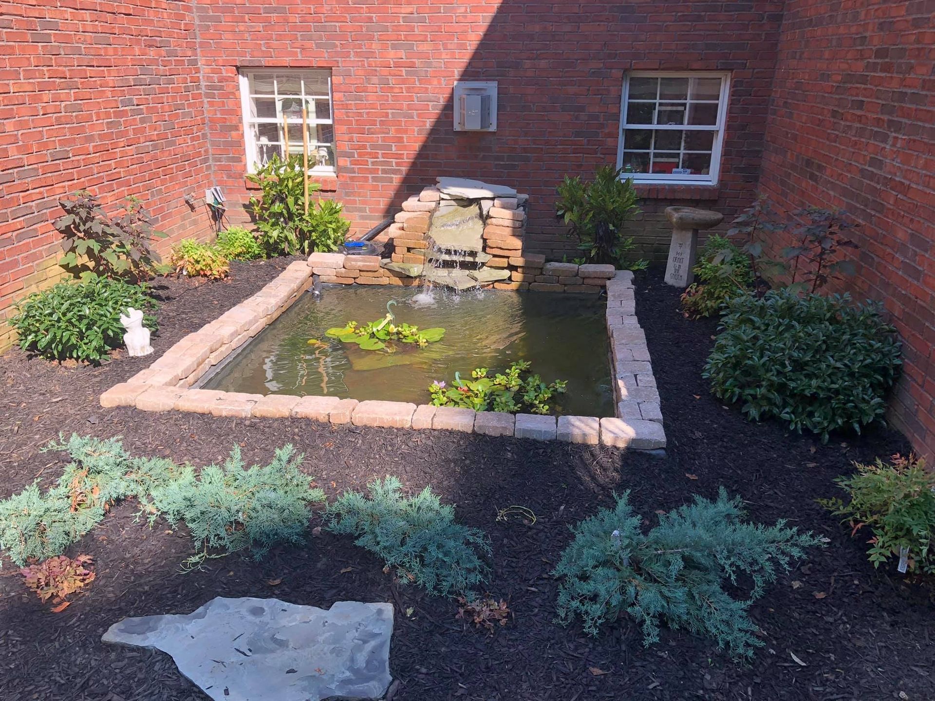A small pond in the middle of a garden in front of a brick building