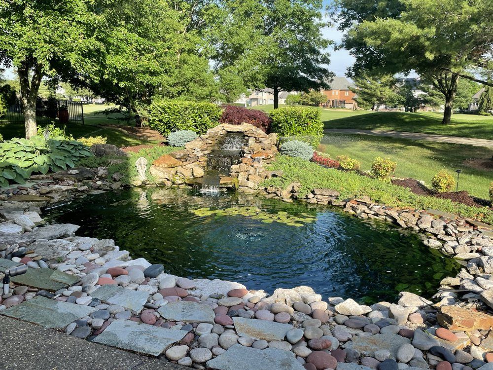 A pond with a waterfall in the middle of a park.